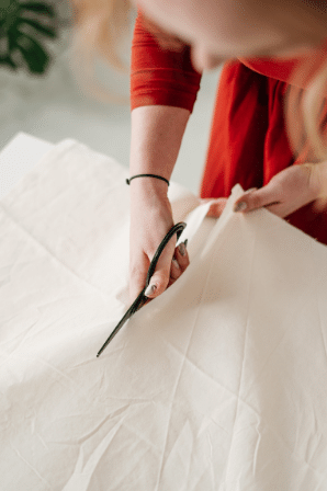 Mulher cortando pedaço de pano branco com uma tesoura